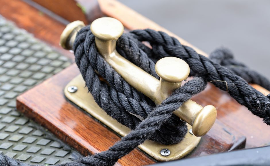 Brass boat cleat with rope on varnished wood deck